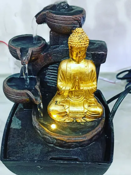 This tabletop water fountain features a golden Buddha and a multi-tiered water flow. The gentle sound of water is perfect for creating a relaxing indoor atmosphere.