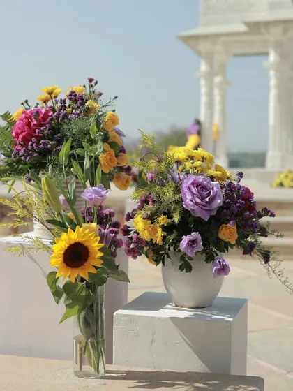 A beautiful arrangement of sunflowers and purple roses, with the white marble pillars of the mandap in the background.