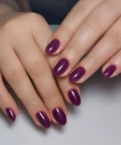 A simple yet elegant manicure with a deep, glossy plum polish on oval-shaped nails.