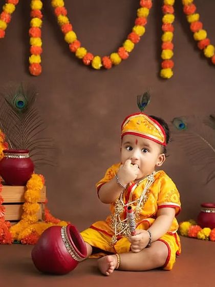 A baby dressed as Krishna curiously tastes the "butter" from the pot.