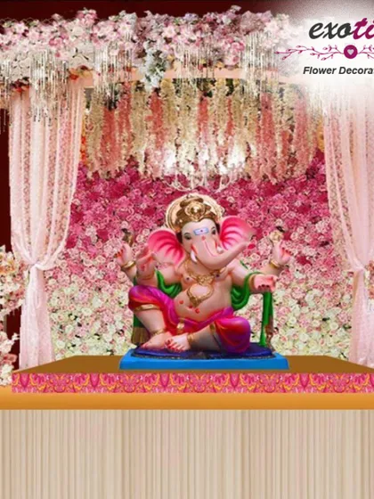 An opulent Ganpati mandap design. This setup features a backdrop of pink roses, a canopy of hanging florals, and sheer pink drapes for a grand and royal look.
