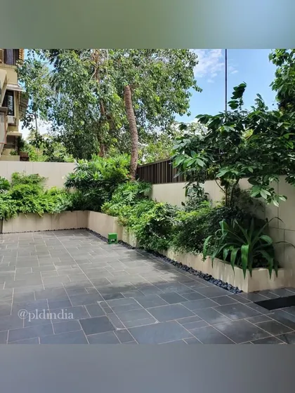 A simple paved patio is surrounded by raised planters filled with dense greenery. This design creates a private, enclosed garden space perfect for a small family gathering.