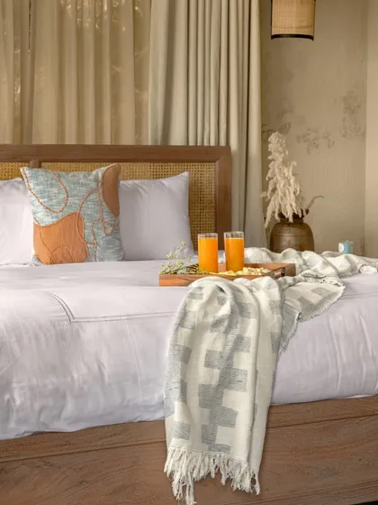 A close-up of the bed, showing the simple, high-quality linens and the natural textures of the woven cane headboard. Every detail is chosen to complement the serene, wabi-sabi aesthetic of the mountain retreat.