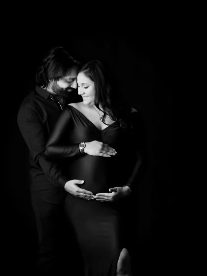 An elegant black and white maternity portrait that uses dramatic, low-key lighting to create a timeless and intimate feel. This studio shot focuses on the beautiful form of the baby bump.