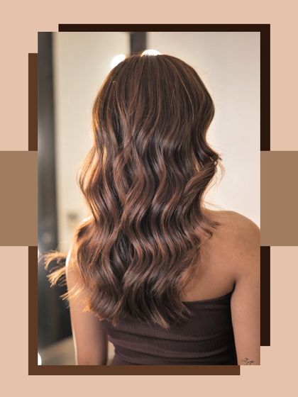 A beautiful shot of a chocolate brown hair colour with subtle caramel highlights. The hair is styled in loose, glamorous waves.
