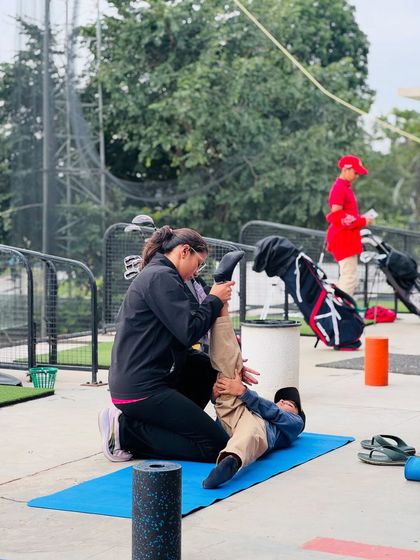 A physiotherapist assists a junior golfer with a post-round stretch. We teach our athletes the importance of recovery from a young age.