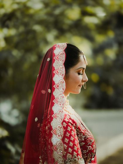A serene profile shot of a bride in her red lehenga, her eyes closed, surrounded by nature.