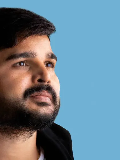 A close-up headshot of a male model against a clean blue background. The lighting is focused to highlight facial features and create a thoughtful expression, perfect for a portfolio.