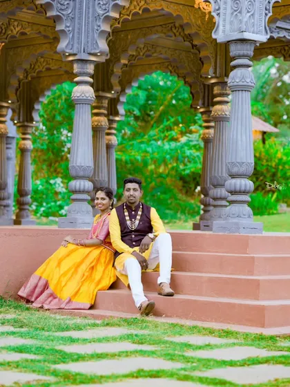 A relaxed moment on the steps of a stone gazebo. The couple's colorful ethnic wear contrasts beautifully with the neutral stone and green grass.