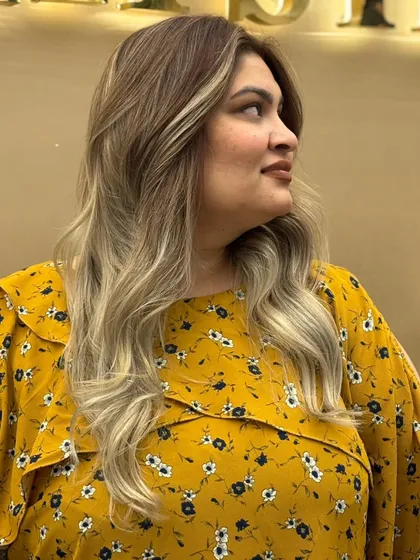 A side view of a client's balayage hair color, styled with soft waves to enhance the dimension and movement of the look.
