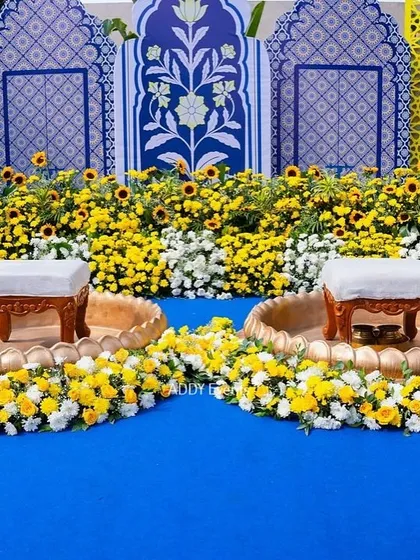 The main seating area for a Greek-inspired Haldi, with a backdrop of blue and yellow jaali panels and urlis filled with sunflowers.