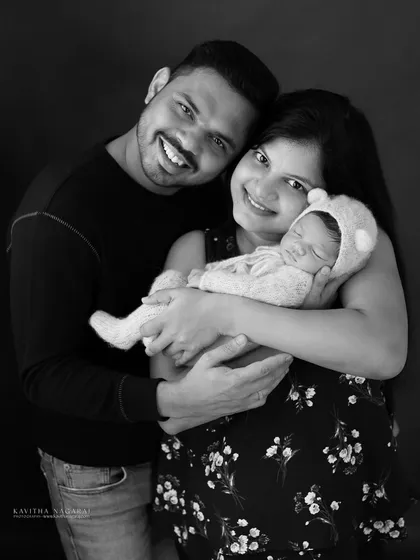 A beautiful family of three, smiling and happy. The parents hold their newborn, dressed in a cute bear outfit, creating a warm and loving first family portrait.