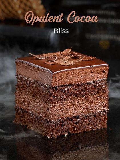 Meet the Opulent Cocoa Bliss, a multi-layered chocolate pastry. It combines dense chocolate sponge with silky chocolate mousse and is topped with delicate chocolate shavings for a rich and satisfying experience.
