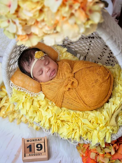 A newborn rests in a hanging chair prop decorated with yellow flowers. The calendar block marks the special day, adding a personal touch to the portrait.