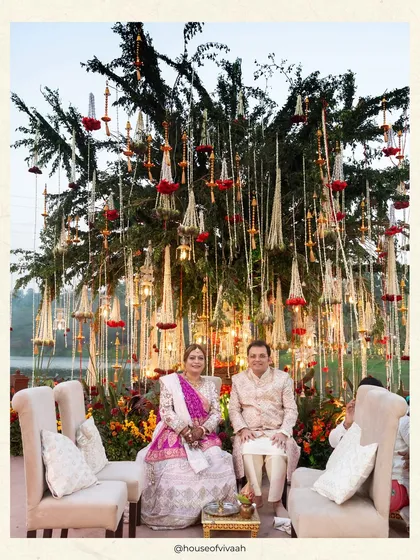 The bride's family seated before a magnificent tree adorned with hanging mogra and rose tassels, creating a unique and natural backdrop for the wedding ceremony.