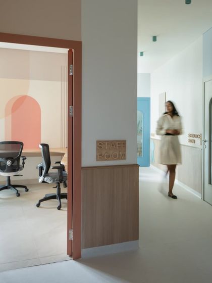 A peek into a staff room from the corridor. The use of soft colors and wooden signage creates a professional yet welcoming environment for the teachers and staff.