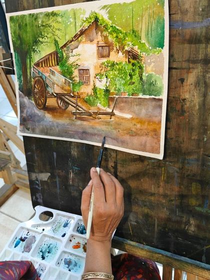 A close-up of the artist's hand and brush, adding the final touches to her watercolor painting.
