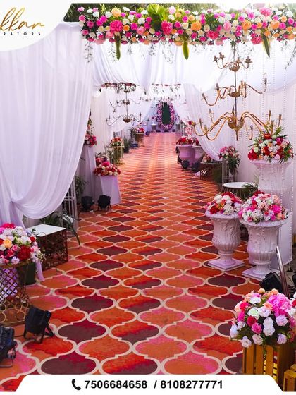 A grand wedding requires a grand entrance. This long, patterned aisle is flanked by floral arrangements and chandeliers, leading guests through a beautiful passage of white drapes.