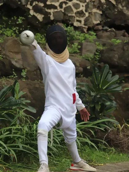 A young fencer in full gear, practicing their form outdoors. We encourage our athletes to find strength and inspiration from their surroundings.