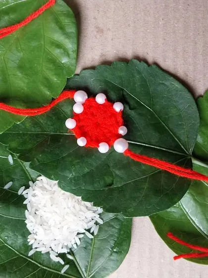 A red rakhi with delicate white pearl embellishments.