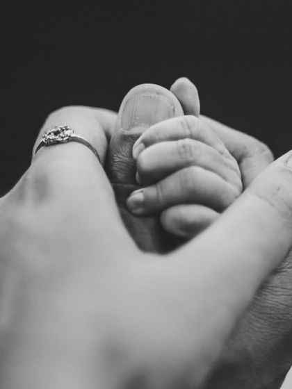A newborn's hand held securely by both parents. This black and white detail shot is a beautiful representation of family, love, and the protection that surrounds a new baby.