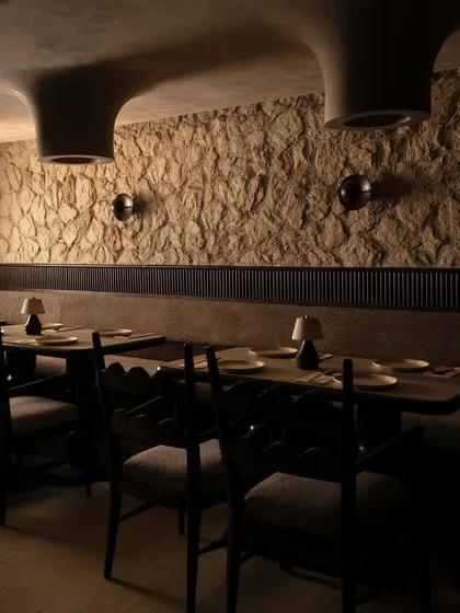 The main dining level, where the texture of the stone wall is highlighted by soft, ambient lighting. The seating arrangement follows the organic curves of the architecture, creating a natural and comfortable flow.