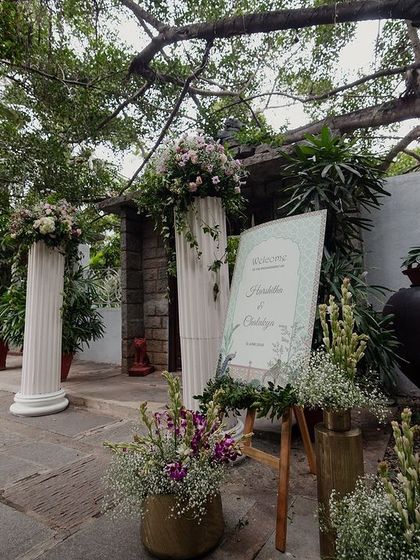 The welcome area decor, featuring white pillars, floral arrangements, and a custom sign.