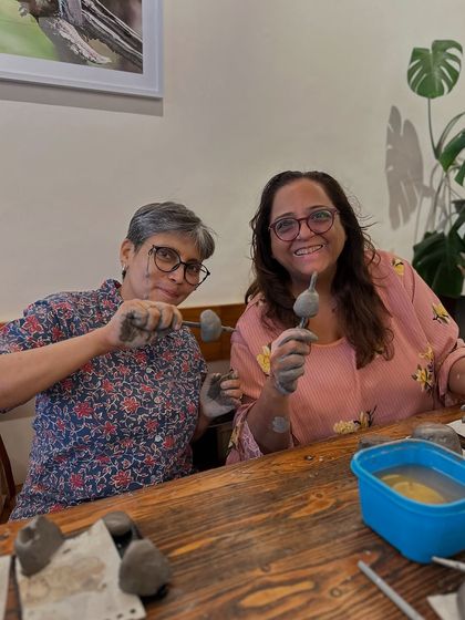 Two friends proudly showing off their works-in-progress during a sculpting workshop. It's all about having fun and not being afraid to get a little messy.