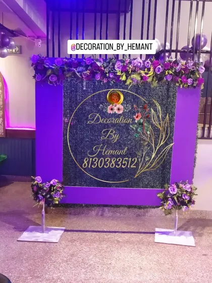 A unique photo backdrop featuring a green grass wall with a purple frame. The top is adorned with purple flowers, and a custom gold-acrylic sign with my brand name is placed in the center.