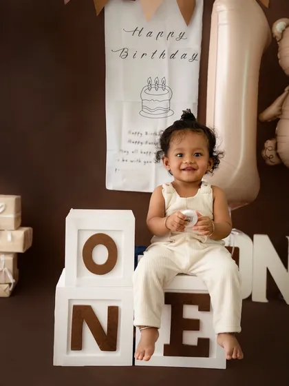 A classic first birthday portrait. This little one's bright smile shines in a charming, neutral-toned setup featuring "ONE" blocks and a sweet teddy bear theme.