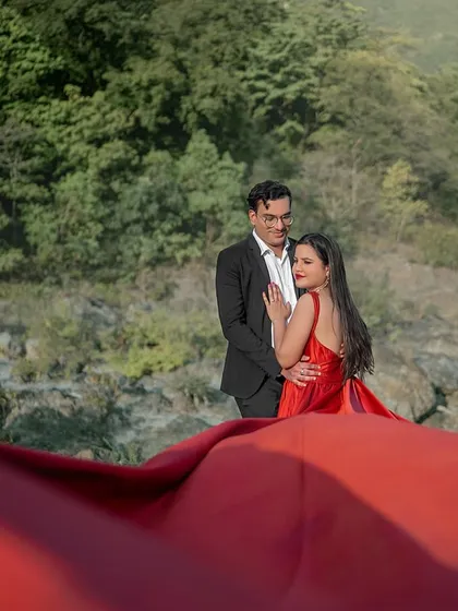Using the flowing red fabric to frame the couple, this shot creates a sense of intimacy and drama. The river and mountains in the background add to the epic scale of this cinematic pre-wedding photo.