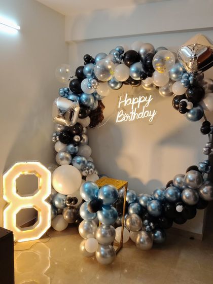 A modern and stylish setup for an 8th birthday, using a cool palette of black, silver, and metallic blue. The decoration features a full balloon ring, a neon sign, and a large light-up number '8'.