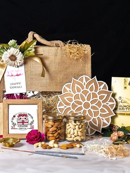 This professionally shot image highlights a beautiful Diwali hamper featuring a jute bag, a box of sweets, cookies, a decorative mandala, and jars of nuts. It's a perfect example of a balanced gift that combines traditional and contemporary elements.