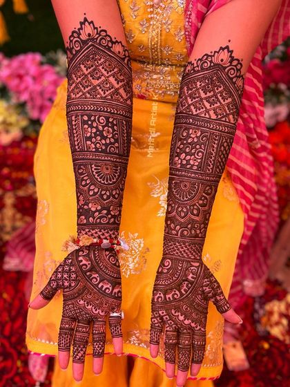 A beautiful shot of full bridal mehndi against a colorful wedding backdrop. The design features traditional architecture and intricate filler patterns.