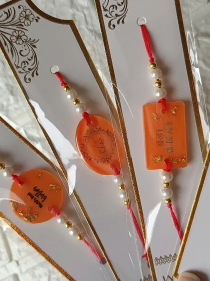 These beautiful orange rakhis are decorated with gold flakes and personalized with messages like 'World's Best Bro'. They are all handmade and ready for the festival.