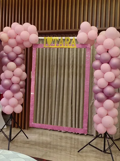 A fun selfie booth is a great addition to a naming ceremony. This one features a custom pink frame flanked by matching balloon pillars, giving guests a dedicated spot to capture fun photos and memories.