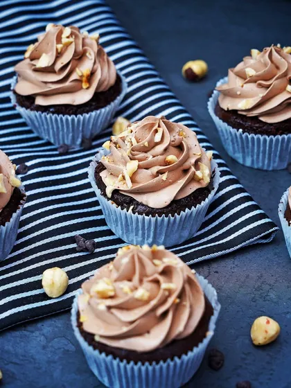 A group of chocolate hazelnut cupcakes with perfectly swirled frosting, shot on a dark, textured surface. This image emphasizes the rich, decadent quality of the dessert.