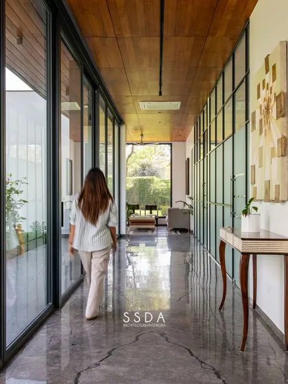 In 'The Green Axis' office, a linear corridor doubles as a contemplative lounge space. The design is intentionally minimal, with a wooden ceiling and glass walls that frame views of the courtyard, promoting a sense of calm and focus.