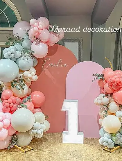 This modern first birthday setup uses two arched backdrops in contrasting colors. The scene is decorated with a pastel organic balloon garland and a large, illuminated number '1'.