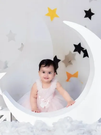 A sweet portrait of a baby girl in a pink dress, posing on our crescent moon prop for her first birthday photoshoot.