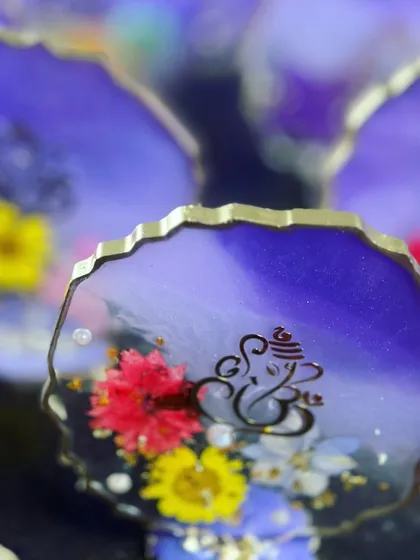 A close up look at one of my personalized Ganesha wedding favors. You can see the delicate dried flowers and the shimmering gold Ganesha motif against the purple and white resin swirl.