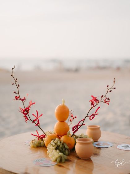 A small, artistic centerpiece of oranges and flowers on a cocktail table at the beach.