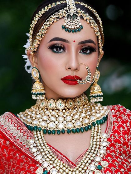 A stunning bride in a classic red lehenga, wearing a full Kundan and green bead rental set.