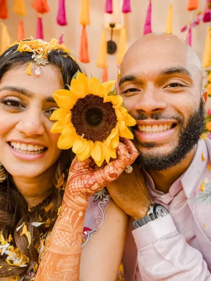 A bright and happy portrait from a Haldi ceremony. The use of a sunflower adds a cheerful and symbolic touch to this joyful moment.