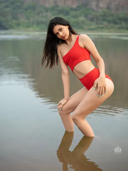 A dynamic pose in a red swimsuit, with the model looking back at the camera. The water and the natural setting create a fresh and energetic feel.