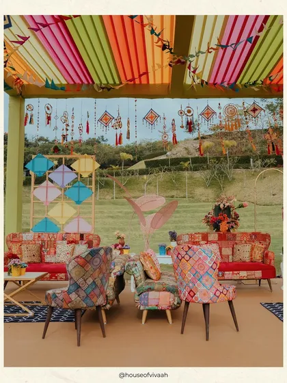 A cozy lounge area at the Kite Carnival, with colorful patchwork furniture set under a canopy of vibrant drapes and hanging kite-themed decor.