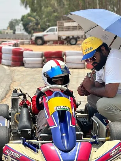 A coach kneels down to talk strategy with a young driver, providing personalized instruction under the shade of an umbrella.
