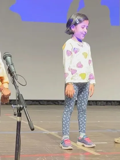 Three students practice their scene on stage, complete with a microphone, showing the confidence they build through performance.