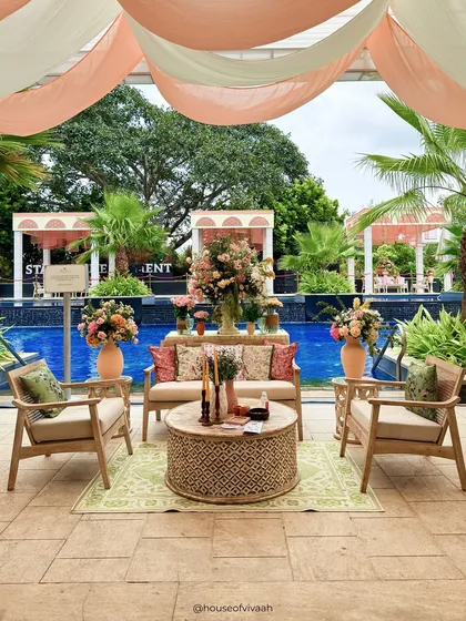 A beautiful poolside lounge area under a canopy of peach and white drapes, with natural cane furniture and vibrant floral arrangements creating a relaxed yet luxurious vibe.