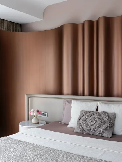 A close-up of the master bedroom in 'The House of Arcs', showing the subtle contrast of textures between the metallic headboard, soft pillows, and smooth bedside table.